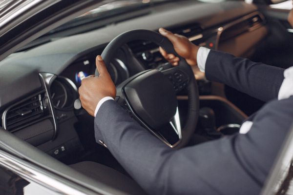 Man buying the car. Businessman in a car salon. Black male in a suit.