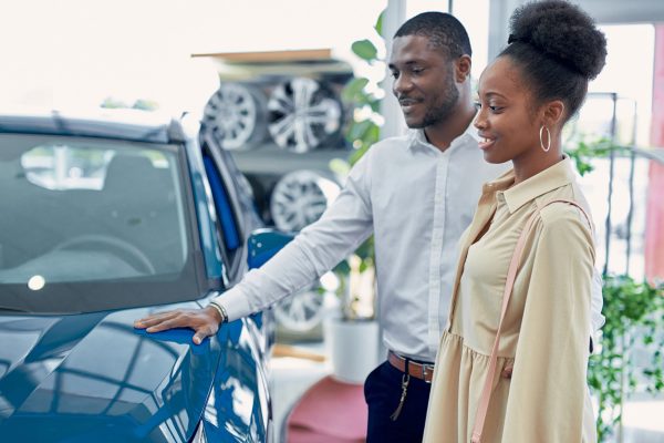 just imagine us on the road. portrait of happy african american couple checking out a car in modern dealership, they choose new car together