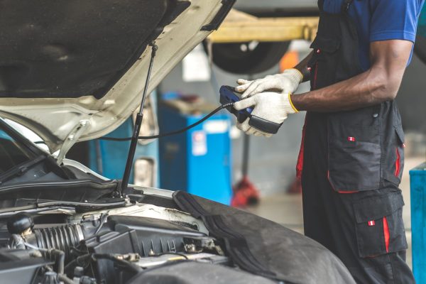 Professional car mechanic repair service and checking car engine by Diagnostics Software computer. Expertise mechanic working in automobile repair garage.